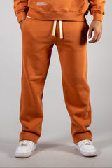 Model wearing the blaze orange AFLETE New Era tracksuit 001, joggers front view